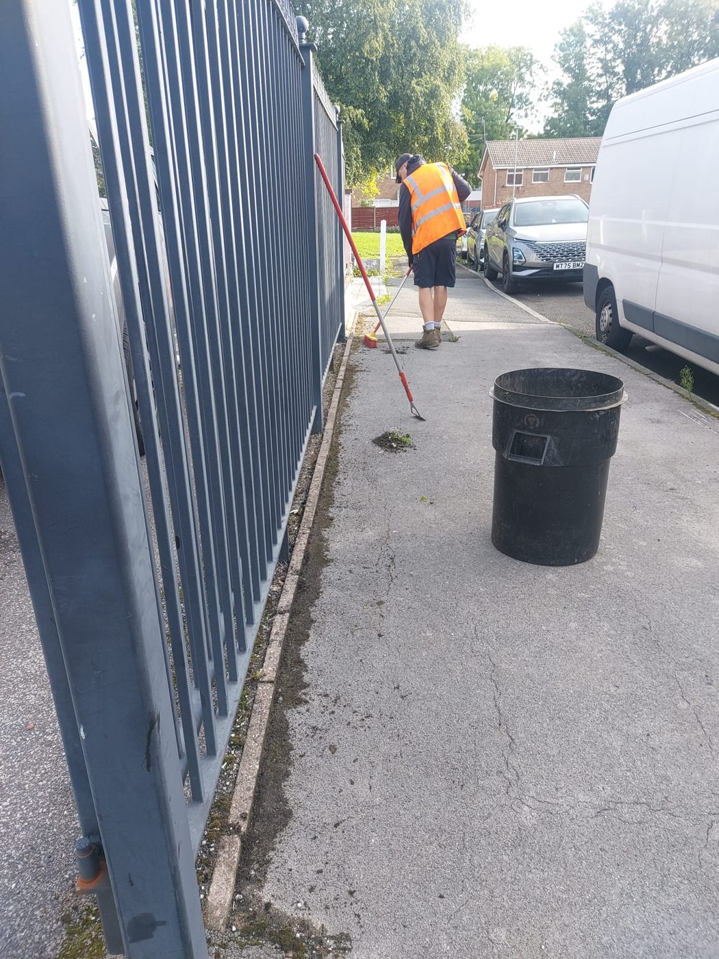 Grounds maintenance operative sweeping along a metal fence
